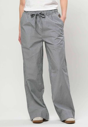 Personne portant un pantalon ample à rayures verticales noires et blanches avec une taille à cordon et des chaussures blanches.