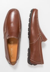 Brune læderskinds slip-on sko med kontrastsyninger, rund tå og gummisål med struktureret greb. Logo synligt indvendigt.