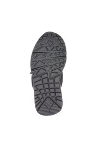 Musta kumipohja kengästä, jossa on geometrisia kuvioita, kuten kolmioita, suorakulmioita ja teksturoitu kanta valkoista taustaa vasten.