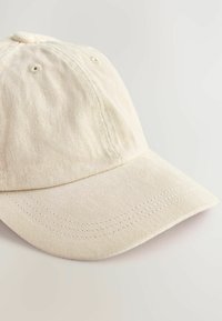 Beige bomuldsbaseballkasket med en rund krone, syet skygge og to ventilationshuller på siderne. Glat stofstruktur.