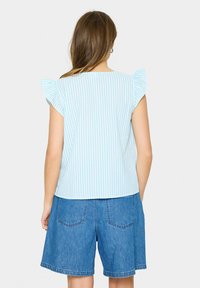 Top a righe blu chiaro e bianco con maniche a volant, abbinato a pantaloni shorts in denim blu con tasche posteriori e vestibilità comoda.