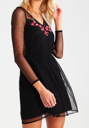 Robe noire avec manches longues en voile transparent à pois, ornée de broderies florales sur le corsage et d'une taille froncée. Tissu léger et texturé.