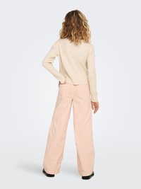 Kreminės spalvos megztinis su siaurėjančiomis detalėmis ir ilgomis rankovėmis, derinamas su rausvais, platėjančiais, aukšto liemens kelnėmis. Juodi kulkšnies aulinukai užbaigia aprangą.