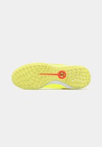 Suela texturizada en amarillo y naranja de una zapatilla deportiva con patrones de agarre circulares sobre un fondo blanco.