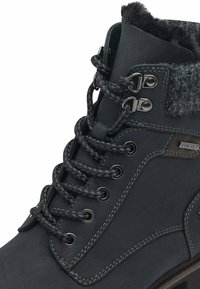 Botín de cuero negro hasta el tobillo con forro de borreguillo gris, que presenta ojales de metal, cordones trenzados y un detalle de costura en gris en contraste.