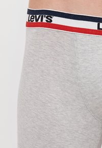 Sivi pamučni bokserice s širokim pojasom koji sadrži plave, crvene i bijele pruge, te "Levi's" logotip. Glatka tekstura i prilagođeni oblik.