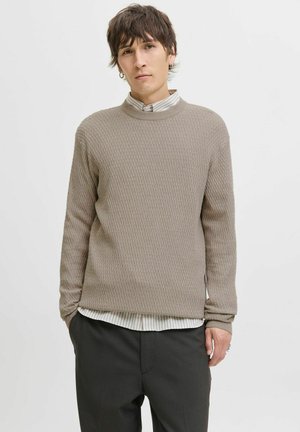 Beige gemêleerde trui met een hoge nek en lange mouwen, gedragen over een wit en grijs gestreept shirt, gecombineerd met zwarte broek.
