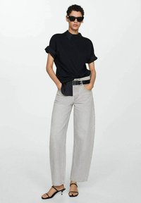 Svart kortärmad skjorta med krage, ljusgrå högmidjade vida jeans och svarta sandaler med remmar. Enkelt, rent design.