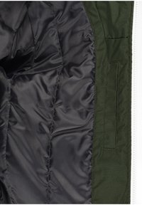 Interno della giacca verde con fodera nera liscia. Presenta una tasca laterale e un design trapuntato. Chiusura a zip lungo il bordo destro.