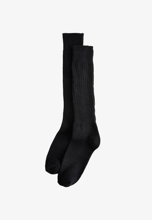 Paire de longues chaussettes noires côtelées, placées côte à côte sur un fond blanc, montrant leur longueur complète du bord à la pointe.