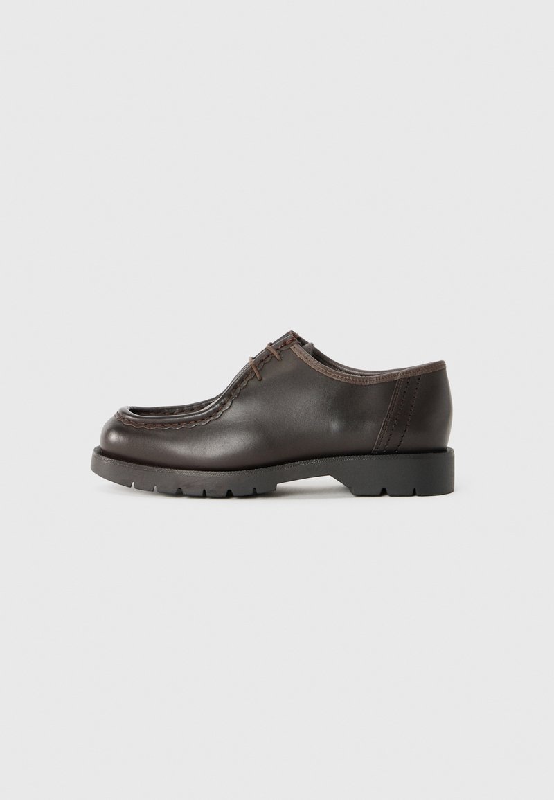 Donkerbruin leren veterschoen met dikke zwarte zool en gedetailleerde stiksels langs de bovenranden, zijaanzicht op een lichte achtergrond.