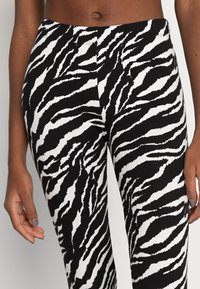 Leggings con stampa zebra bianca e nera, dal tocco morbido, con design aderente e vita elastica. Vista ravvicinata, mani appoggiate sui fianchi.
