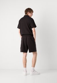 Set di polo nera e pantaloni corti. Tessuto morbido, maniche corte, vita elastica, tasche laterali, abbinato a scarpe e calzini di colore chiaro.