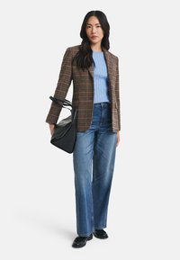 Blazer i brun rutete stoff, blå kabelstrikket genser, vide blå denimjeans og svart strukturert veske med to håndtak. Svarte sko.