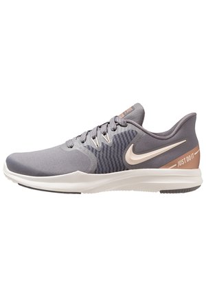 Szary niski but do biegania Nike z białą podeszwą, białym logo Nike i napisem "Just Do It" na pięcie w jasnobrązowym kolorze.