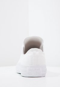 Weiße Low-Top Converse All Star Sneaker von hinten auf einer weißen Oberfläche mit einem schlichten weißen Hintergrund gezeigt.