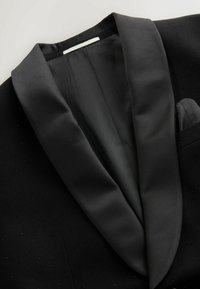 Sacou negru de smoking, cu guler din satin, țesătură texturată cu puncte decorative mici și o singură buzunar pe piept, echipat cu un batiste.