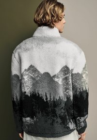Kurtka polarowa z górskim krajobrazem w odcieniach szarości, czerni i bieli. Posiada wysoki kołnierz oraz fakturowany materiał.