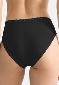 Hooggeknipte zwarte onderbroek van zacht materiaal met geschulpte kantafwerking rond de tailleband en een gladde, naadloze rand.