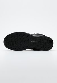 Suela de zapato de senderismo negro con goma texturizada para agarre, que presenta un diseño de banda de rodadura con patrón y una marca visible en el centro.
