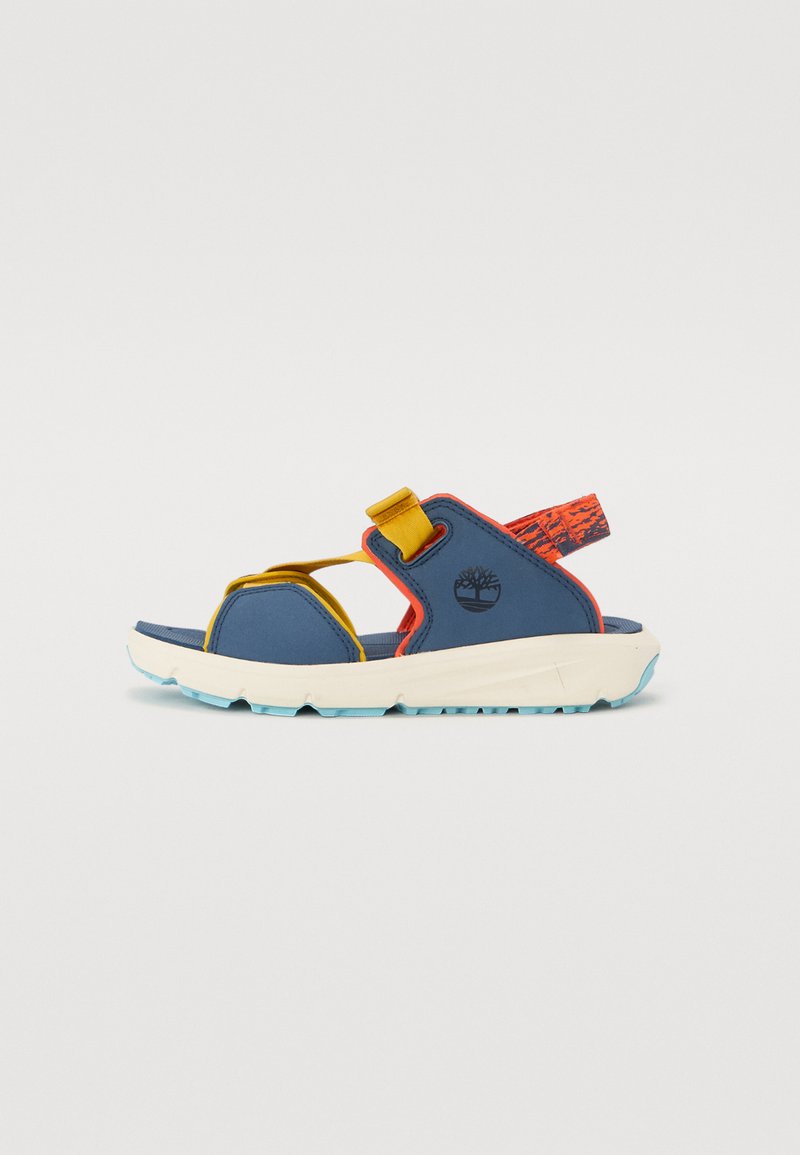 Blå sandal med gule og røde detaljer, justerbare stropper, en teksturert oransje hælflik og en hvit såle med et blått mønster.