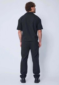 Chemise noire à manches courtes associée à un pantalon assorti ; coupe décontractée, en coton, sans logos ni motifs visibles, portée avec des chaussures noires imposantes.