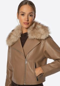 Tan lederen cropped jack met een bontkraag, voorzien van een ritssluiting aan de voorkant, zijzakken en een gladde textuur. Accenten zijn stiksels.