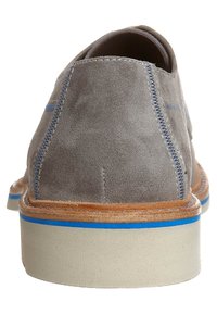 Scarpa casual da uomo in suede grigio vista dal retro, con cuciture blu, rifiniture marroni e una suola bianca spessa con una striscia blu.