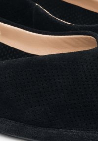 Czarne wsuwane buty wykonane z perforowanej skóry zamszowej z gładkim beżowym podszyciem. Charakteryzują się zaokrąglonymi krawędziami i teksturowaną czarną podeszwą.