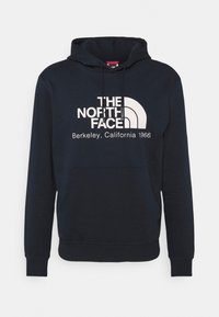 Námořnická modrá mikina s kapucí a přední kapsou, s bílým logem "The North Face Berkeley, California 1966" a grafikou oblouku na hrudi.