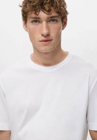 Biała bawełniana koszulka z okrągłym dekoltem, krótkimi rękawami i gładką fakturą, o klasycznym kroju i czystym wzornictwie.