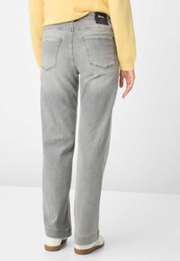 Pantaloni in denim grigio chiaro con vestibilità a gamba dritta, due tasche posteriori e un'etichetta nera in vita. Indossati con sneakers bianche.