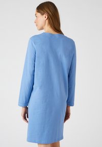 Robe en coton bleu avec des manches longues, un col rond et des accents de boutons décoratifs aux poignets. Coupe simple et décontractée avec une texture lisse.