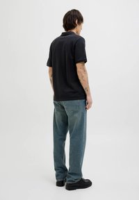 Polo shirt nero in cotone, con colletto classico e maniche corte, abbinato a jeans blu a taglio comodo e scarpe nere.