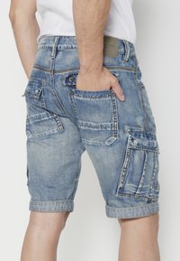Vaaleansiniset farkku cargo-shortsit, joissa on haalistunut pinta, useita taskuja ja käännetty helma. Takakatsaus, jossa näkyy ompelu- ja taskutiedot.