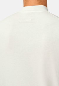 Helles graues Rundhals-Sweatshirt mit einer glatten Textur. Verfügt über ein kleines, weißes Markenlabel am Halsausschnitt. Der Stoff wirkt weich und komfortabel.