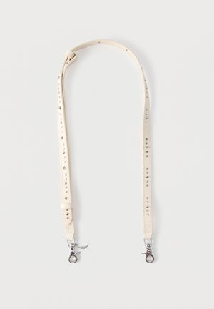 Ρυθμιζόμενο μπεζ δερμάτινο λουράκι με μεταλλικά κλιπ και διακοσμητικές μεταλλικές καρφίτσες σε απλό φωτεινό φόντο.