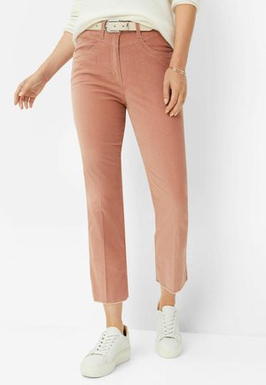 Samtpantalons in sanftem Rosa, lässiger Schritt-Design, mit Fronttaschen und passendem Gürtel. Kombiniert mit weißen Sneakers.