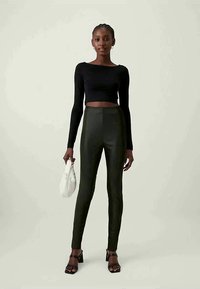 Μαύρο μακρυμάνικο crop top συνδυασμένο με ψηλόμεσα σκούρα πράσινα κολάν. Το μοντέλο κρατά μια μικρή λευκή τσάντα, φορώντας μαύρες με λουριά γόβες.