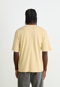 Beige katoenen t-shirt met korte mouwen, ontspannen pasvorm en een ronde hals. Eenvoudig ontwerp, zachte textuur en een gladde achterkant.