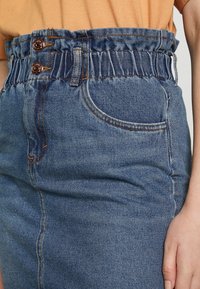Jupe en denim avec une taille élastique froncée, dotée de deux boutons en bronze, de couleur bleu clair et d'un design classique à cinq poches.