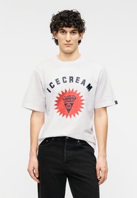 Λευκό κοντομάνικο t-shirt με στρογγυλή λαιμόκοψη, με τον έντονο γράφο "ICECREAM" σε ναυτικό μπλε και κόκκινο, καθώς και σχέδιο ρόμβου. Συνδυάζεται με μαύρο τζιν.