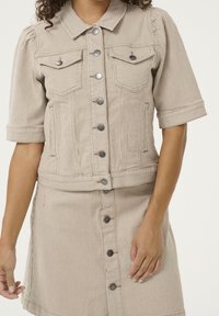 Beigen raidallinen farkkutakki, jossa on lyhyet hihat, rintataskut ja metalliset napit, yhdistettynä vastaavaan hameeseen, jossa on nappikiinnitys.