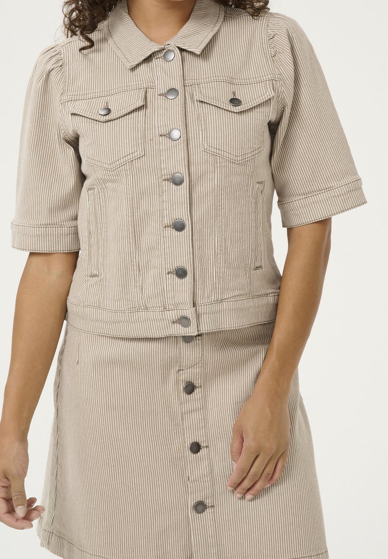 Beigen raidallinen farkkutakki, jossa on lyhyet hihat, rintataskut ja metalliset napit, yhdistettynä vastaavaan hameeseen, jossa on nappikiinnitys.