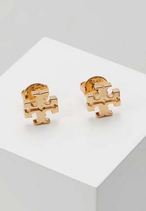 Pendientes de stud en tono dorado que presentan un diseño de pieza de rompecabezas con un acabado pulido y un logo grabado en la parte posterior.