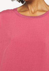 Rosa, kurzärmliges Oberteil mit einem runden Halsausschnitt, glatter Textur und lockerem Schnitt. Das Material scheint weich und atmungsaktiv zu sein.