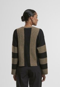 Sweter dzianinowy o krótkim kroju; wyróżnia się wyrazistymi pionowymi paskami w czerni i beżu; teksturowana tkanina z długimi rękawami.