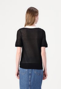 Svart stickad kortärmad tröja med rund halslinning och vit krage, i kombination med en blå denimkjol. Taktile, lättviktig tyg.