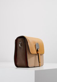 Borsa a tracolla in pelle gialla, beige e marrone. Presenta una finitura testurizzata, chiusura a pattina con un accento metallico circolare e finiture in argento.