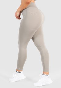 Beige hochtaillierte Leggings, aus dehnbarem Material, mit glatter Textur und enganliegendem Design, kombiniert mit weißen Sportschuhen.